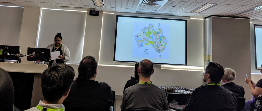 Keynote speaker Jacinta Koolmatrie, speaking in front of audience. Presentation slide on view is the AIATSIS map of Indigenous Australia